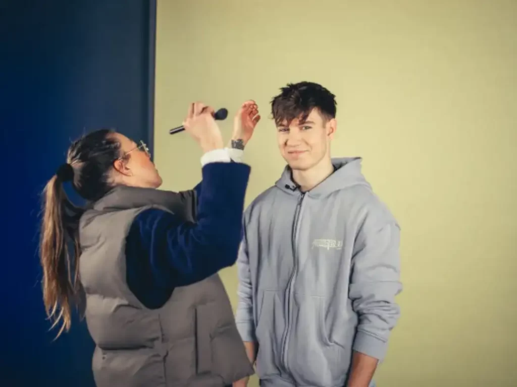 Ein Mann wird auf den Videodreh von einer Maskenbilderin vorbereitet