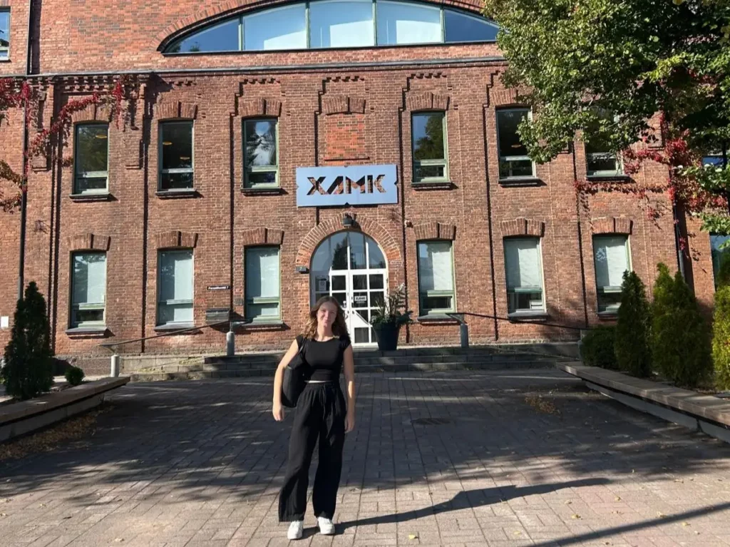 Studentin steht vor dem Hauptgebäude der XAMK University of Applied Sciences in Kouvola, Finnland.