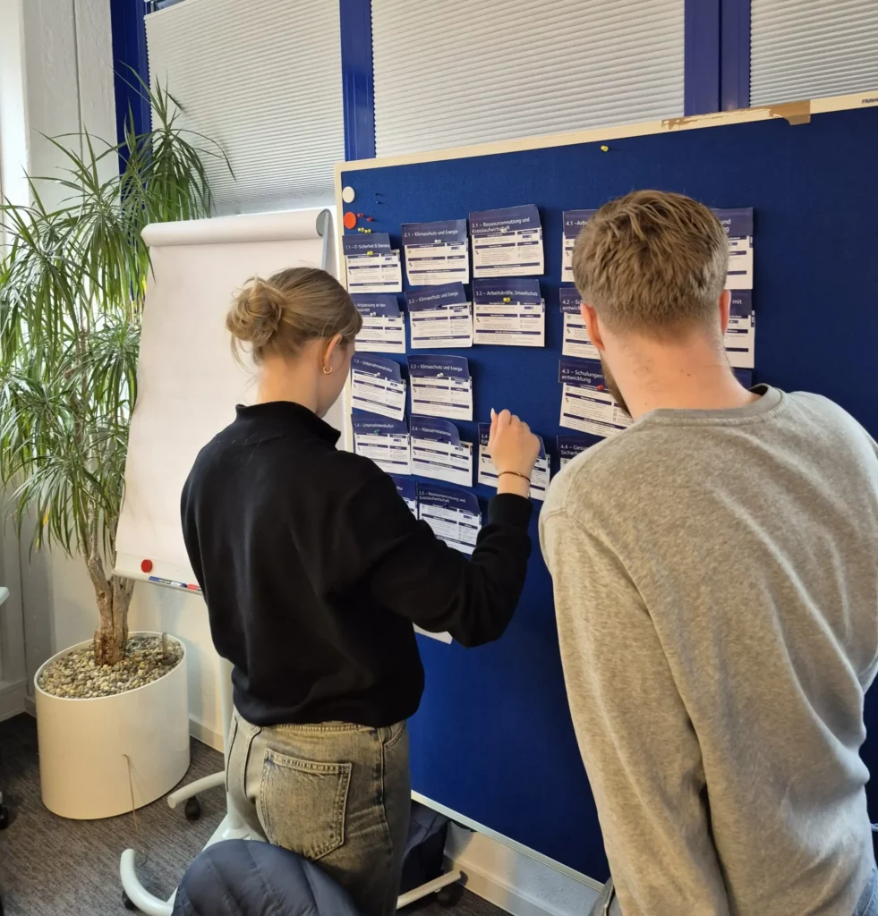 Zwei Azubis befestigen erarbeitete Nachhaltigkeitsideen an einer Pinnwand